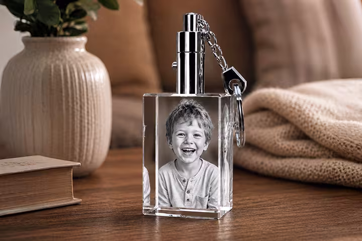 Porte-clés rectangulaire en cristal 2D gravé avec le portrait d’un jeune garçon souriant, doté d’un porte-clés en métal poli, présenté sur une table en bois dans une ambiance chaleureuse.