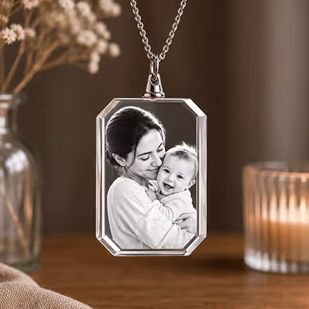 Collier rectangulaire en cristal 2D gravé avec le portrait d’une mère et de son bébé, suspendu à une chaîne en argent à côté d’une bougie allumée.