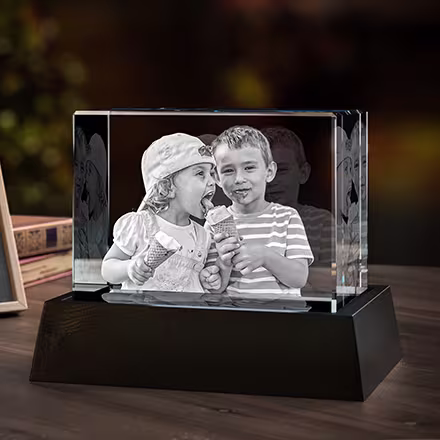 Grand cristal photo 3D rectangulaire gravé avec la photo de deux enfants partageant une glace, présenté sur une base lumineuse LED noire à côté de la photo originale.